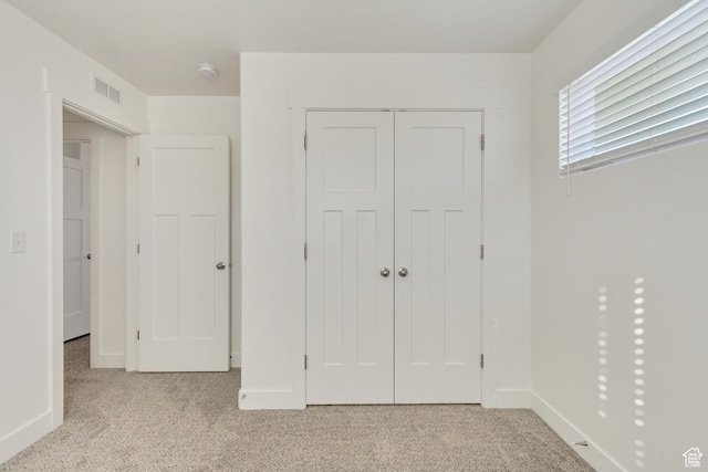 unfurnished bedroom with light colored carpet and a closet