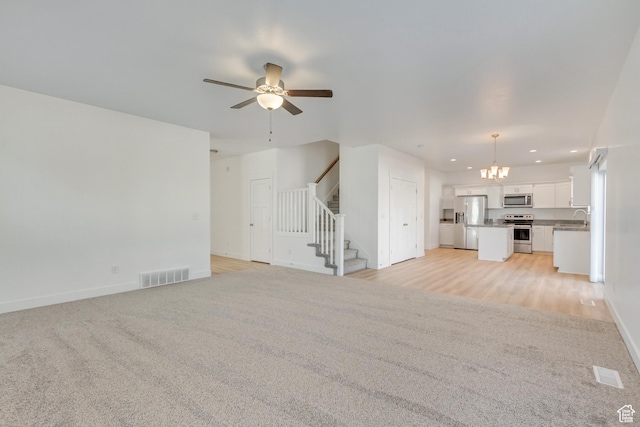 unfurnished living room featuring light carpet, ceiling fan with notable chandelier, and sink