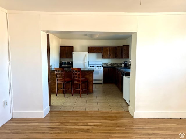 kitchen featuring dark brown cabinets, white appliances, sink, and light hardwood / wood-style flooring