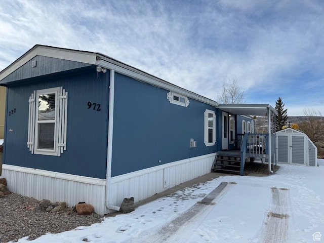 snow covered property featuring a wooden deck and a storage shed