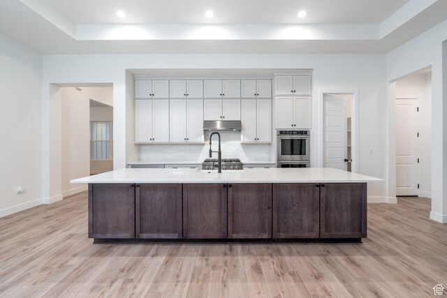 kitchen with a large island with sink, white cabinetry, stainless steel double oven, and light wood-type flooring