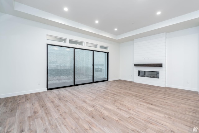 unfurnished living room featuring a large fireplace, light hardwood / wood-style floors, and a tray ceiling