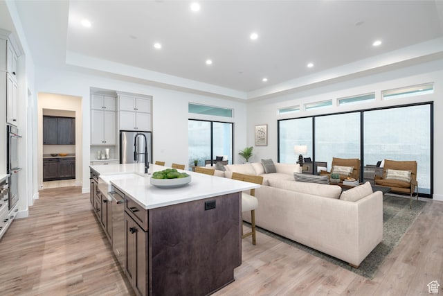 kitchen with dark brown cabinetry, white cabinetry, light hardwood / wood-style flooring, a kitchen island with sink, and a breakfast bar