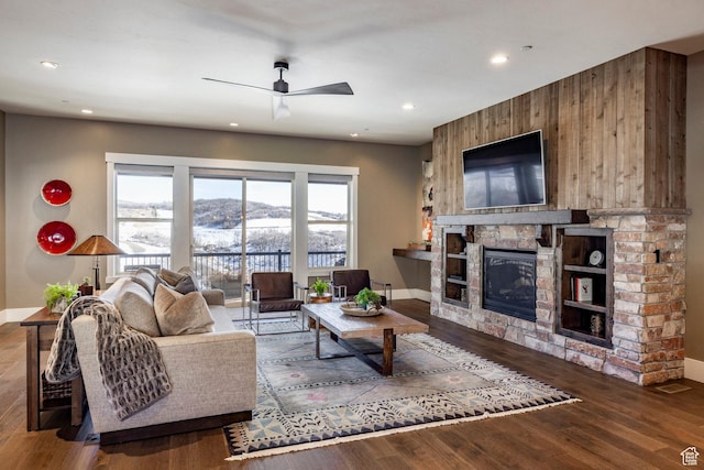 living room with a stone fireplace, ceiling fan, and wood-type flooring