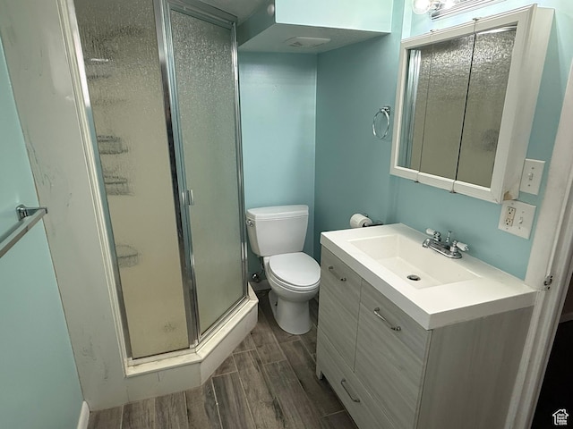 bathroom featuring visible vents, toilet, wood tiled floor, a shower stall, and vanity
