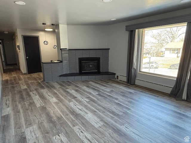 unfurnished living room with a baseboard heating unit, a brick fireplace, and wood finished floors