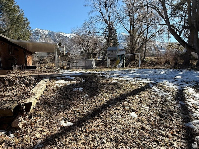 snowy yard featuring an attached carport, a playground, and a mountain view