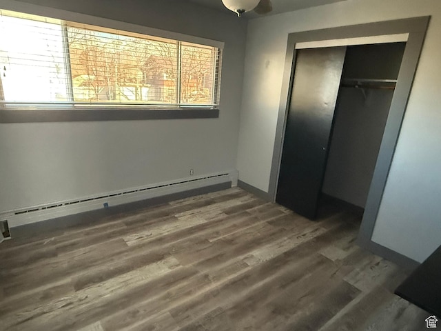 unfurnished bedroom with a baseboard radiator, a closet, baseboards, and wood finished floors