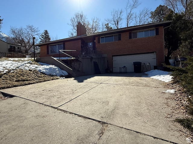 view of front of house featuring concrete driveway, brick siding, a chimney, and an attached garage