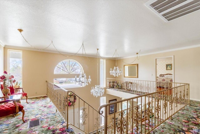 corridor with a notable chandelier, ornamental molding, a textured ceiling, and a wealth of natural light