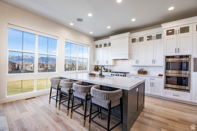 kitchen with a mountain view, stainless steel double oven, white cabinetry, and a kitchen island with sink