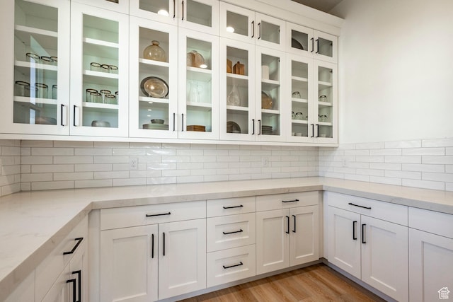 kitchen with white cabinetry, backsplash, light stone countertops, and light hardwood / wood-style flooring