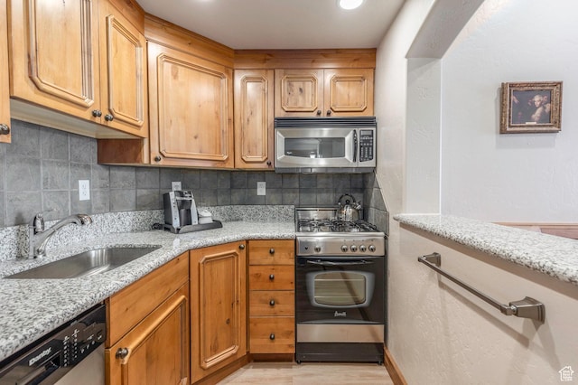 kitchen with sink, light stone countertops, stainless steel appliances, and tasteful backsplash
