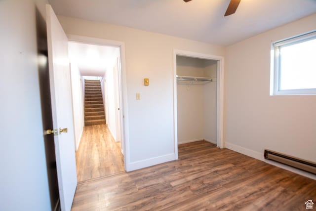 unfurnished bedroom featuring hardwood / wood-style floors, a closet, baseboard heating, and ceiling fan