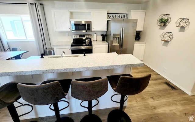 573 S Aspen Dr, Garden City, UT 84028 - kitchen featuring stainless steel appliances, white cabinetry, a breakfast bar area, and light hardwood / wood-style flooring