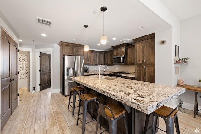 13579 N Hillclimb Ln, Kamas, UT 84036 - kitchen featuring light stone counters, an island with sink, pendant lighting, light hardwood / wood-style floors, and appliances with stainless steel finishes