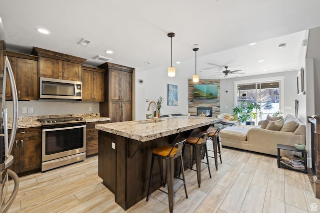 13579 N Hillclimb Ln, Kamas, UT 84036 - kitchen featuring a kitchen island with sink, ceiling fan, light stone countertops, light wood-type flooring, and stainless steel appliances