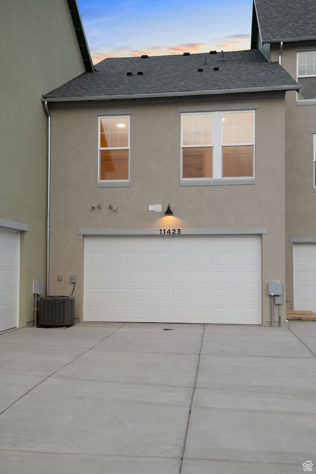 11423 S Watercourse Rd, South Jordan, UT 84009 - back of house at dusk with cooling unit, stucco siding, roof with shingles, and an attached garage