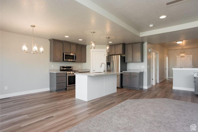 kitchen with a center island with sink, appliances with stainless steel finishes, hanging light fixtures, hardwood / wood-style flooring, and sink