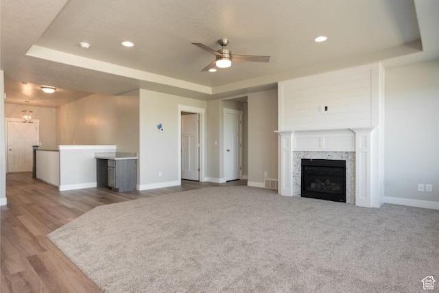 unfurnished living room featuring ceiling fan with notable chandelier, a fireplace, a raised ceiling, and light hardwood / wood-style flooring