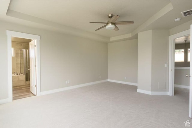 interior space with a raised ceiling, ceiling fan with notable chandelier, light colored carpet, and ensuite bath