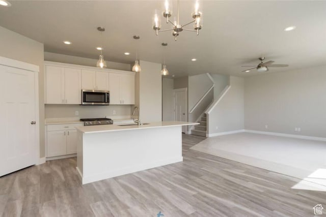 kitchen featuring an island with sink, white cabinets, stainless steel appliances, and decorative light fixtures