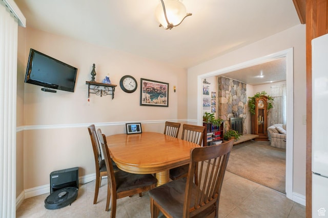 dining room featuring baseboards, a fireplace, light tile patterned floors, and light colored carpet
