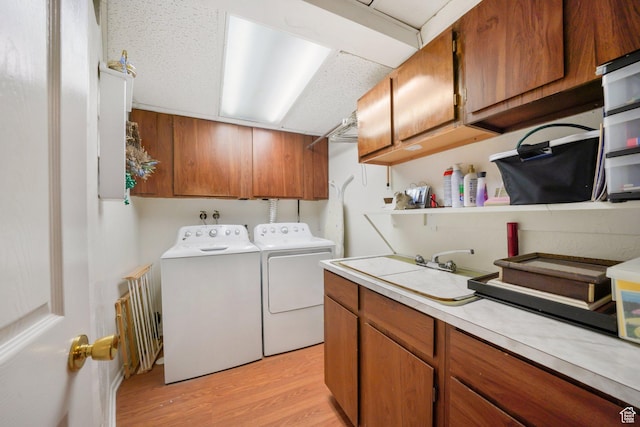 laundry area featuring cabinet space, washer and clothes dryer, light wood finished floors, and a sink