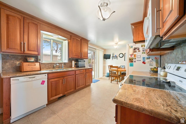 kitchen with brown cabinetry, a sink, and white appliances