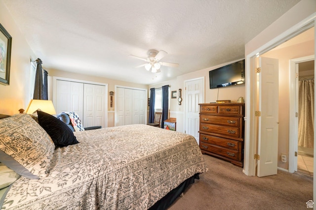 carpeted bedroom with two closets, a ceiling fan, and a textured ceiling