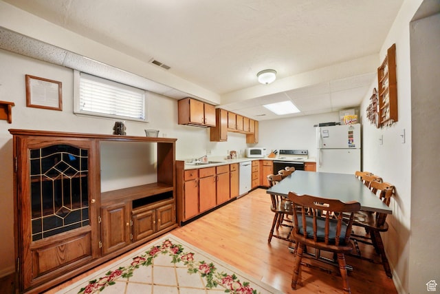kitchen with a sink, light wood-type flooring, visible vents, white appliances, and light countertops