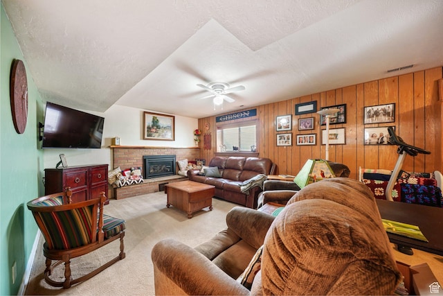 carpeted living area featuring a textured ceiling, ceiling fan, a fireplace, wood walls, and visible vents