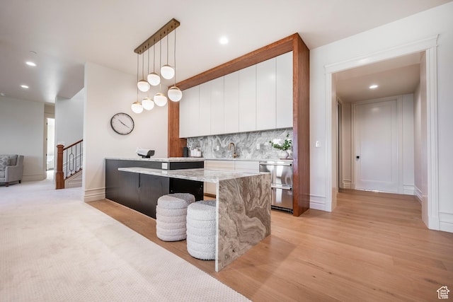 6736 E Via Cortina, Huntsville, UT 84317 - kitchen featuring white cabinets, hanging light fixtures, light hardwood / wood-style flooring, decorative backsplash, and a kitchen bar