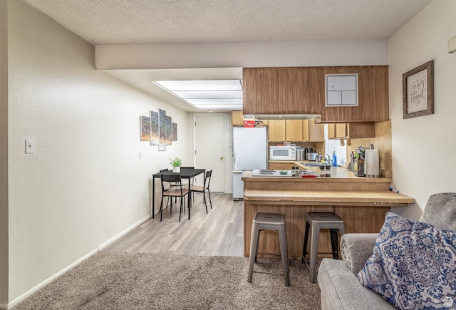 kitchen featuring kitchen peninsula, a kitchen bar, light wood-type flooring, white appliances, and sink