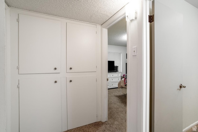 corridor with light colored carpet and a textured ceiling
