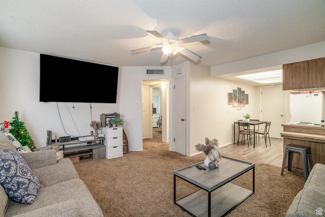 living room featuring light carpet, a textured ceiling, and ceiling fan
