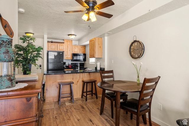 kitchen with black appliances, light wood-style floors, light brown cabinetry, a peninsula, and a textured ceiling