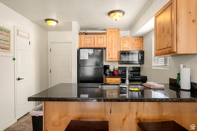 kitchen with black appliances, a peninsula, a breakfast bar area, dark stone counters, and a sink