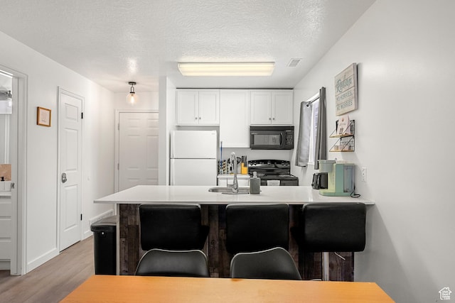 kitchen with black appliances, a sink, light wood-style flooring, a breakfast bar, and white cabinetry