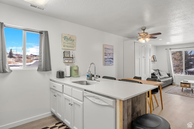 kitchen featuring dishwasher, a sink, a textured ceiling, a peninsula, and plenty of natural light