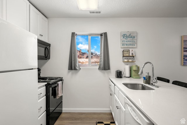 kitchen featuring black appliances, a sink, wood finished floors, light countertops, and a textured ceiling
