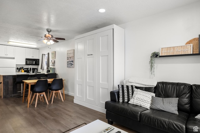 living area with ceiling fan, a textured ceiling, wood finished floors, recessed lighting, and baseboards
