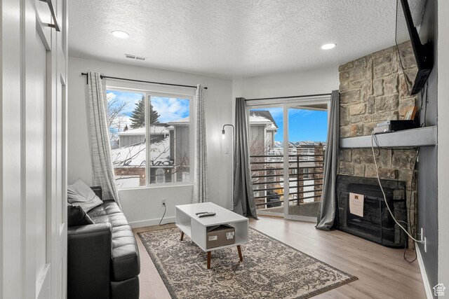 living area featuring a textured ceiling, plenty of natural light, light wood-type flooring, a stone fireplace, and baseboards