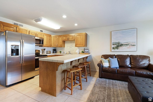 kitchen featuring light tile patterned flooring, sink, a kitchen bar, tile counters, and stainless steel appliances