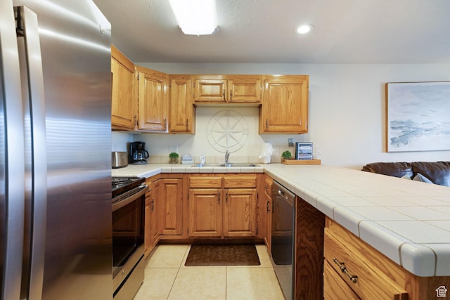 kitchen featuring appliances with stainless steel finishes, tile countertops, sink, light tile patterned floors, and kitchen peninsula