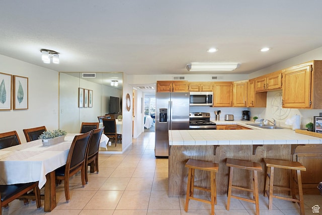 kitchen with appliances with stainless steel finishes, tile countertops, and a breakfast bar