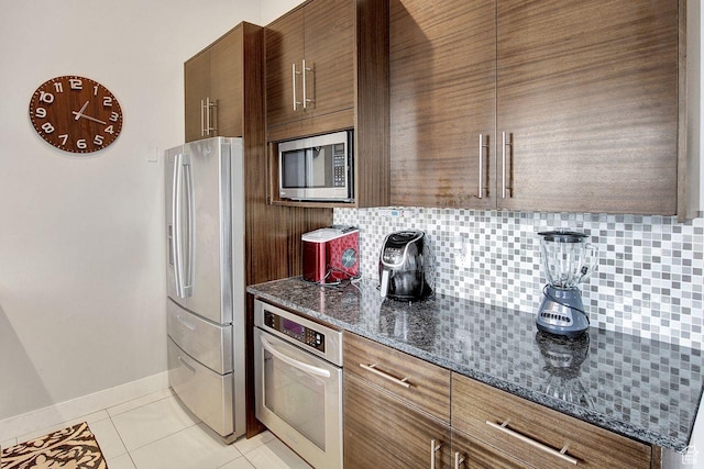 kitchen with dark stone countertops, decorative backsplash, light tile patterned floors, and stainless steel appliances