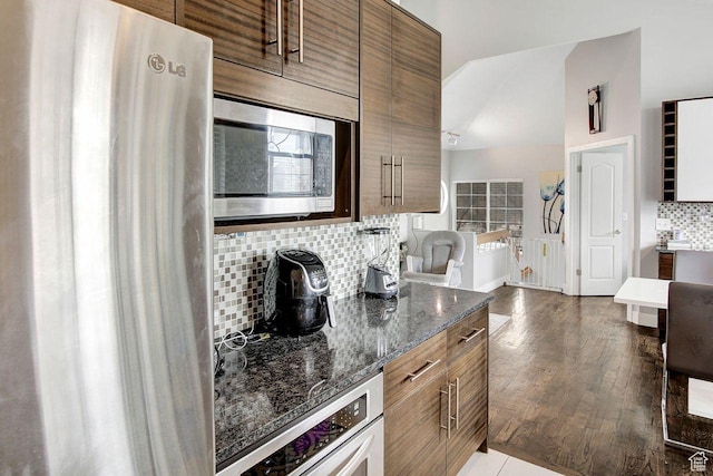 kitchen with decorative backsplash, appliances with stainless steel finishes, dark hardwood / wood-style floors, and dark stone countertops