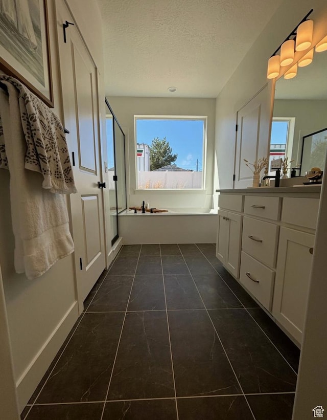 bathroom with vanity, a textured ceiling, a healthy amount of sunlight, and plus walk in shower