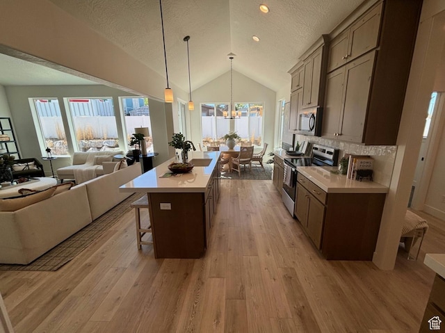 kitchen with a kitchen breakfast bar, vaulted ceiling, appliances with stainless steel finishes, pendant lighting, and tasteful backsplash